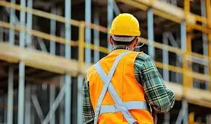 A construction worker wearing a safety vest and hard hat stands